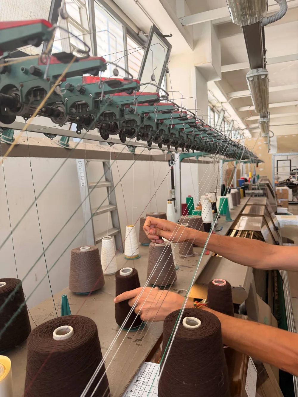 Garnkegel werden an der Strickmaschine eingefädelt